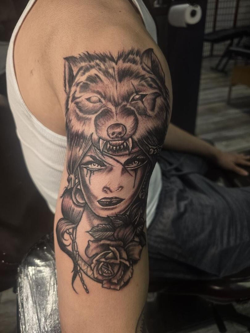 Black-and-grey wolf and woman portrait tattoo on an arm
