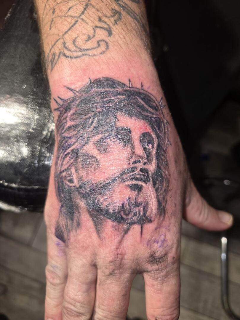 Black-and-grey portrait tattooed on a hand